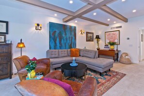 Uma sala de estar moderna com um sofá seccional, poltronas de couro, uma mesa de centro e um grande quadro abstrato.