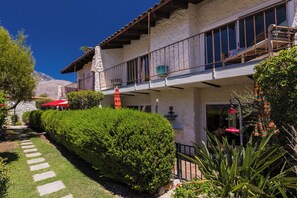 Un edificio de dos pisos con balcón, fachada de piedra y un jardín cuidado con un sendero.