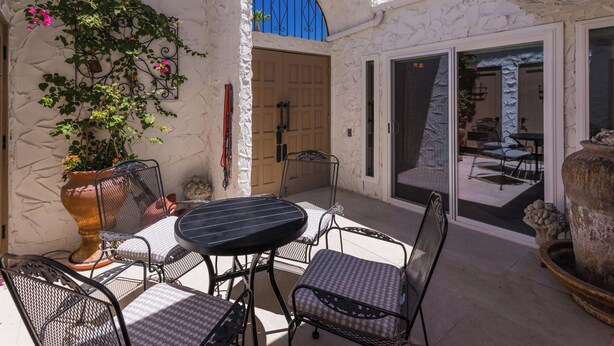 Un patio al aire libre con una mesa y sillas, una planta en maceta y una puerta que da a un espacio interior.