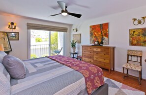 A bedroom with a bed, a dresser, a chair, a ceiling fan, and artwork on the walls. - Stylish Spanish townhome w/ mountain views, pool & spa in South Palm Springs (Palm Springs)