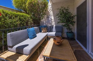 A balcony with a grey sofa, blue cushions, a wooden table, and a potted plant. - Stylish Spanish townhome w/ mountain views, pool & spa in South Palm Springs (Palm Springs)