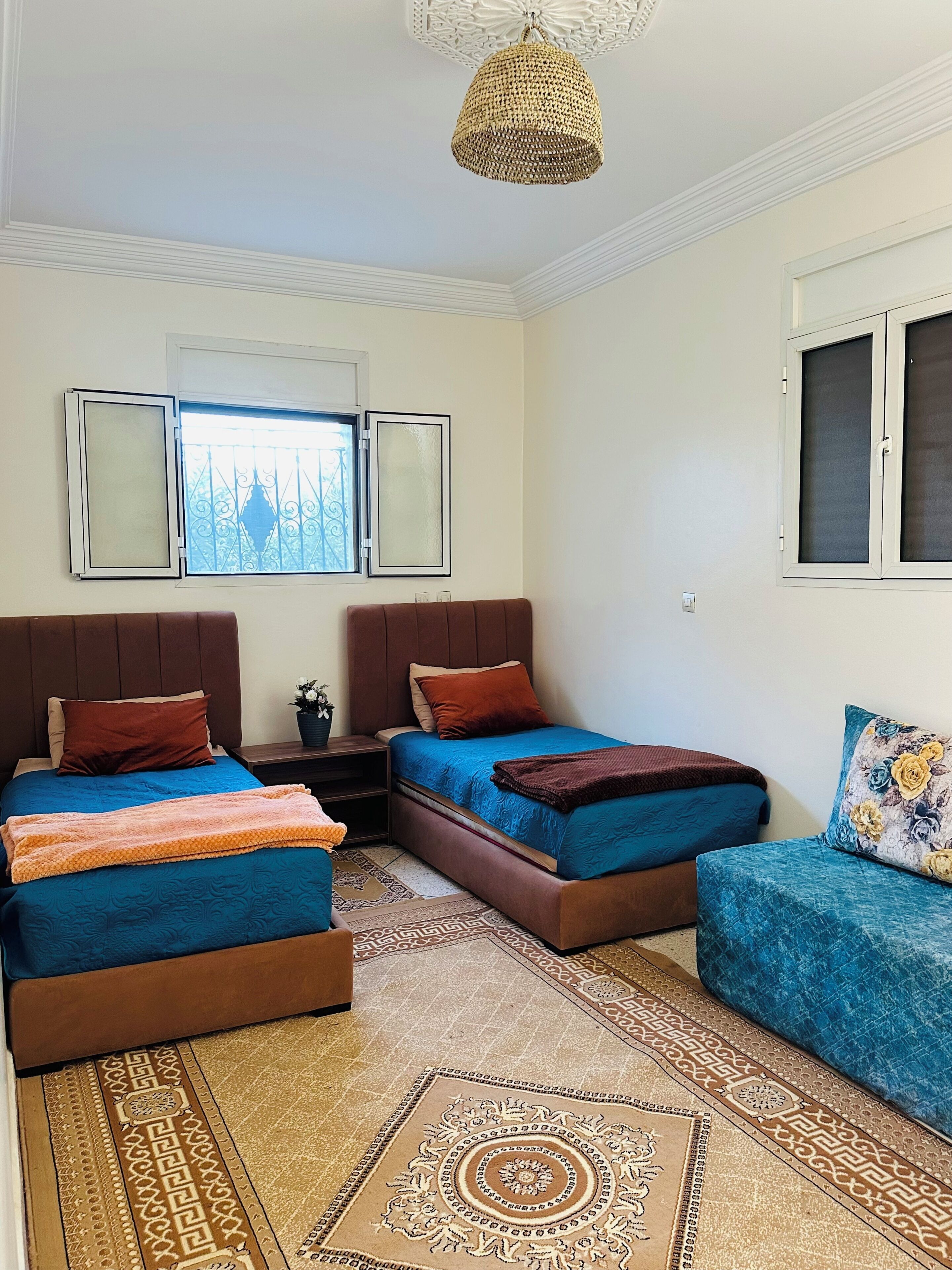 A bedroom with two beds, a sofa, a patterned rug, and a decorative ceiling light.
