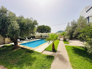 Ein rechteckiger Pool mit Holzterrasse, umgeben von gepflegtem Rasen und Bäumen.