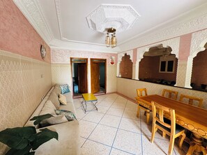 Ein Zimmer mit einer Couch, einem Esstisch, Stühlen und einer Pflanze.