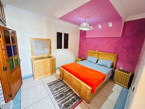 Ein Schlafzimmer mit Bett, Nachttischen, einem Schminktisch und einem Spiegel, sowie einer Deckenleuchte.