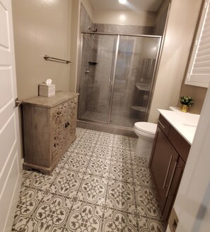A bathroom with a glass-enclosed shower, a toilet, a vanity with a mirror, and patterned floor tiles. - Cozy 1- large bedroom, private bathroom, with mini kitchen, (las vegas)