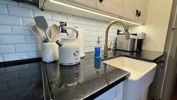 A kitchen with a black countertop, white cabinets, a stainless steel sink, and a kettle.