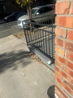 A sidewalk with a metal fence, a tree, and a parked car. - Spacious 3-bedroom apartment with AC in marvelous Brooklyn…. (Brooklyn)
