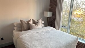 Ett sovrum med en stor säng, en golvlampa och ett fönster med utsikt över träd.