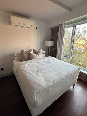 A bedroom with a large bed, a standing lamp, and a window with a view of trees.