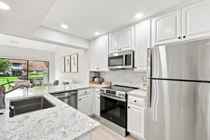 A modern kitchen with white cabinetry, stainless steel appliances, and a marble countertop.