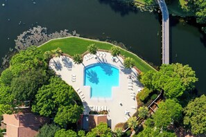 En vy från ovan av en swimmingpool omgiven av grönska och en brygga.