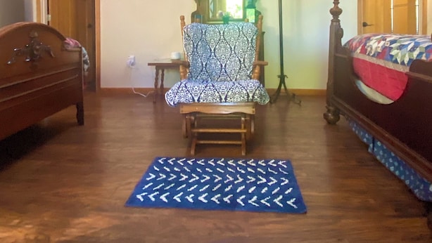 Una habitación con techo alto, una cama de madera, un sillón estampado y una mesita con lámpara.