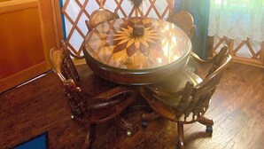 A dining area with a round glass table, chairs, and a decorative shield on the wall.