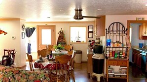 Una sala de estar con un sofá floral, un comedor con mesa y sillas, una cocina con armarios y electrodomésticos, y un ventilador de techo.