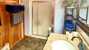 A bathroom with a granite countertop sink, a mirror, a towel rack, a shower door, and a radiator.