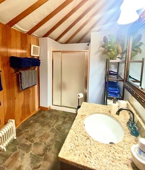 A bathroom with a granite countertop sink, a mirror, a towel rack, a shower door, and a radiator. - Yurtel-Veneta (Veneta)
