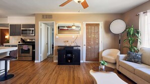A modern living space with a ceiling fan, a kitchen with stainless steel appliances, a dining area with a bar stool, and a seating area with a sofa and a round table. - Backdrop - Private Pool - Mins to Old town (Scottsdale)