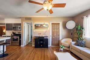 A modern living space with a ceiling fan, a kitchen with stainless steel appliances, a dining area with a bar stool, and a seating area with a sofa and a round table. - Backdrop - Private Pool - Mins to Old town (Scottsdale)