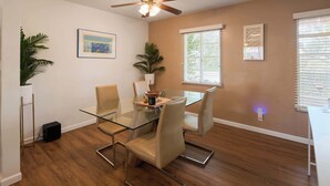 A dining area with a glass table, cushioned chairs, a ceiling fan, and a window with blinds. - Backdrop - Private Pool - Mins to Old town (Scottsdale)