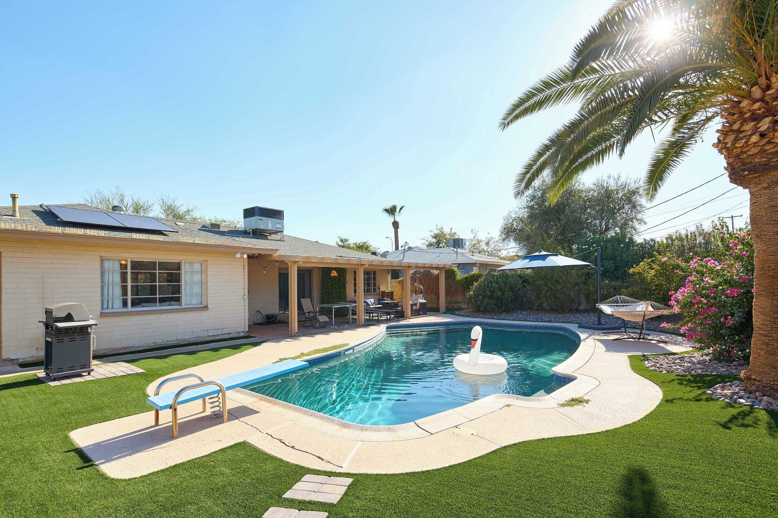 Un patio trasero residencial con piscina, un flotador con forma de cisne y una zona de patio.
