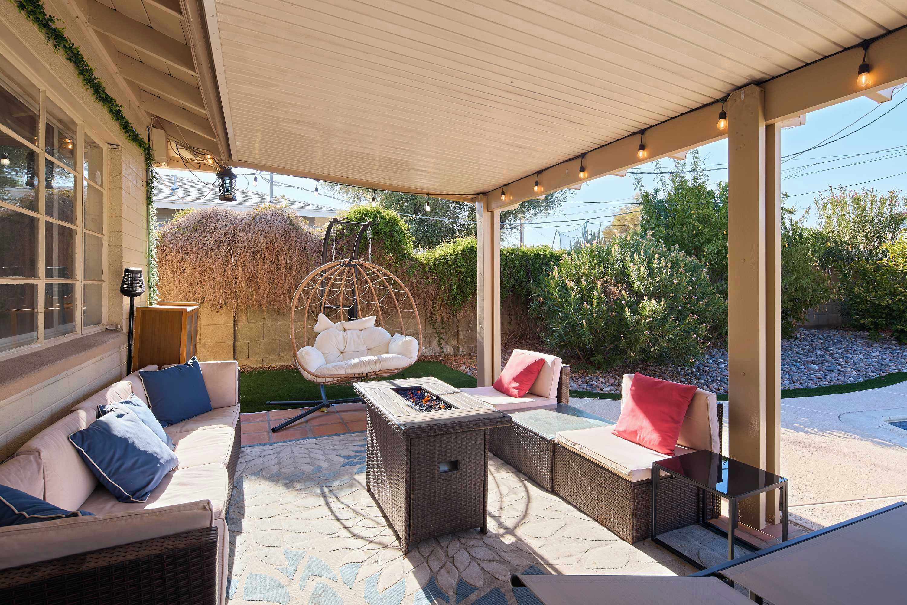 A covered outdoor seating area with wicker furniture, a hanging chair, and a fire pit.
