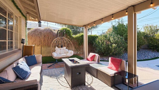A covered outdoor seating area with wicker furniture, a hanging chair, and a fire pit. - Backdrop - Private Pool - Mins to Old town (Scottsdale)