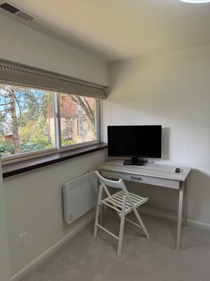 A room with a window, a radiator, a white chair, a desk with a television, and a remote control. - Renovated and private garden apartment near UofU. (Salt Lake City)