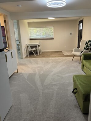 A room with a dining table, chairs, a green sofa, a white armchair, and a window with blinds. - Renovated and private garden apartment near UofU. (Salt Lake City)