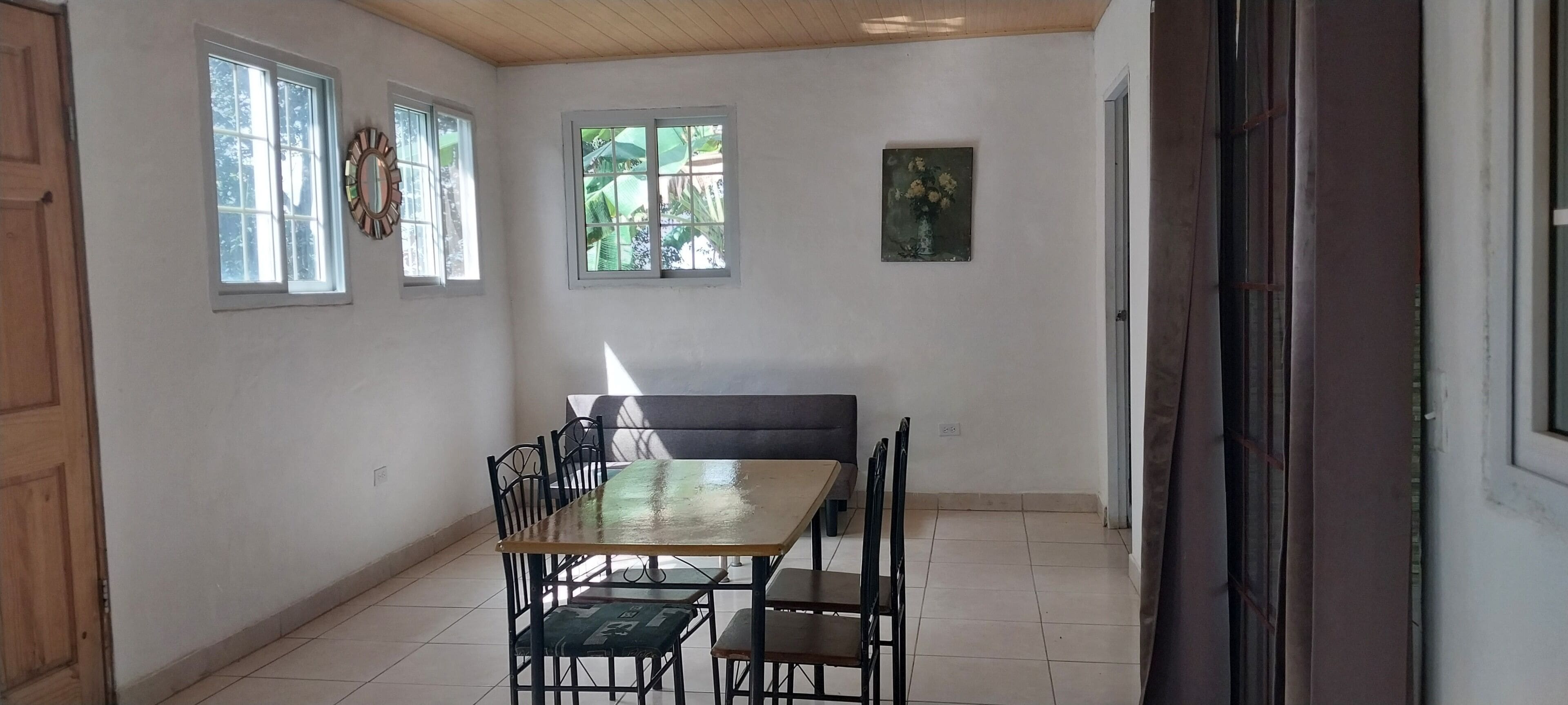 Un espace repas comprenant une table et des chaises, un banc et des fenêtres donnant sur un paysage verdoyant.