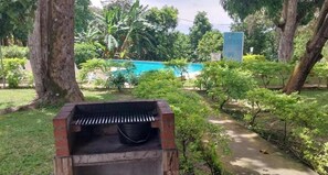 A barbecue grill in a garden with a pool and trees in the background.