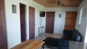 Una habitación con una mesa de madera, un sofá negro y un ventilador de techo.