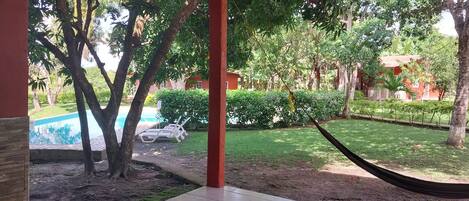 A view of a pool area with a hammock, trees, and a grassy lawn.