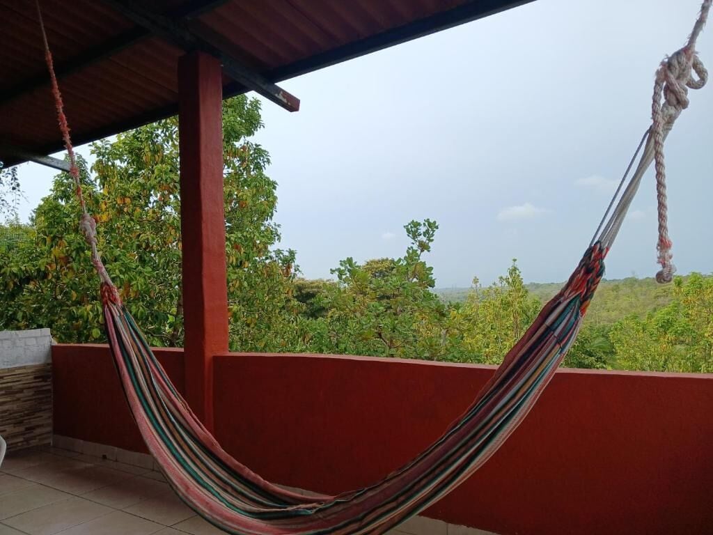 Een hangmat op een balkon met uitzicht op groen en een heldere lucht.