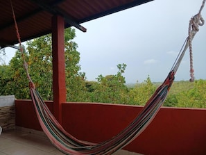 A hammock on a balcony with a view of greenery and a clear sky.