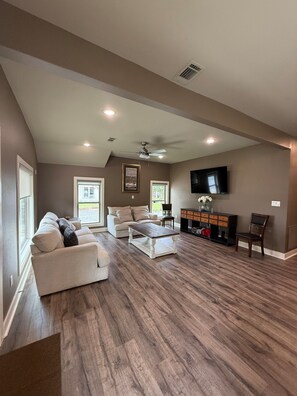 A spacious living room with a high ceiling, a fireplace, and a flat-screen TV mounted on the wall.