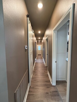 A narrow hallway with a wooden floor, white doors, and recessed ceiling lighting.