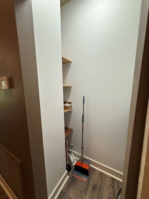 A narrow hallway with a mop leaning against the wall and a broom on the floor.