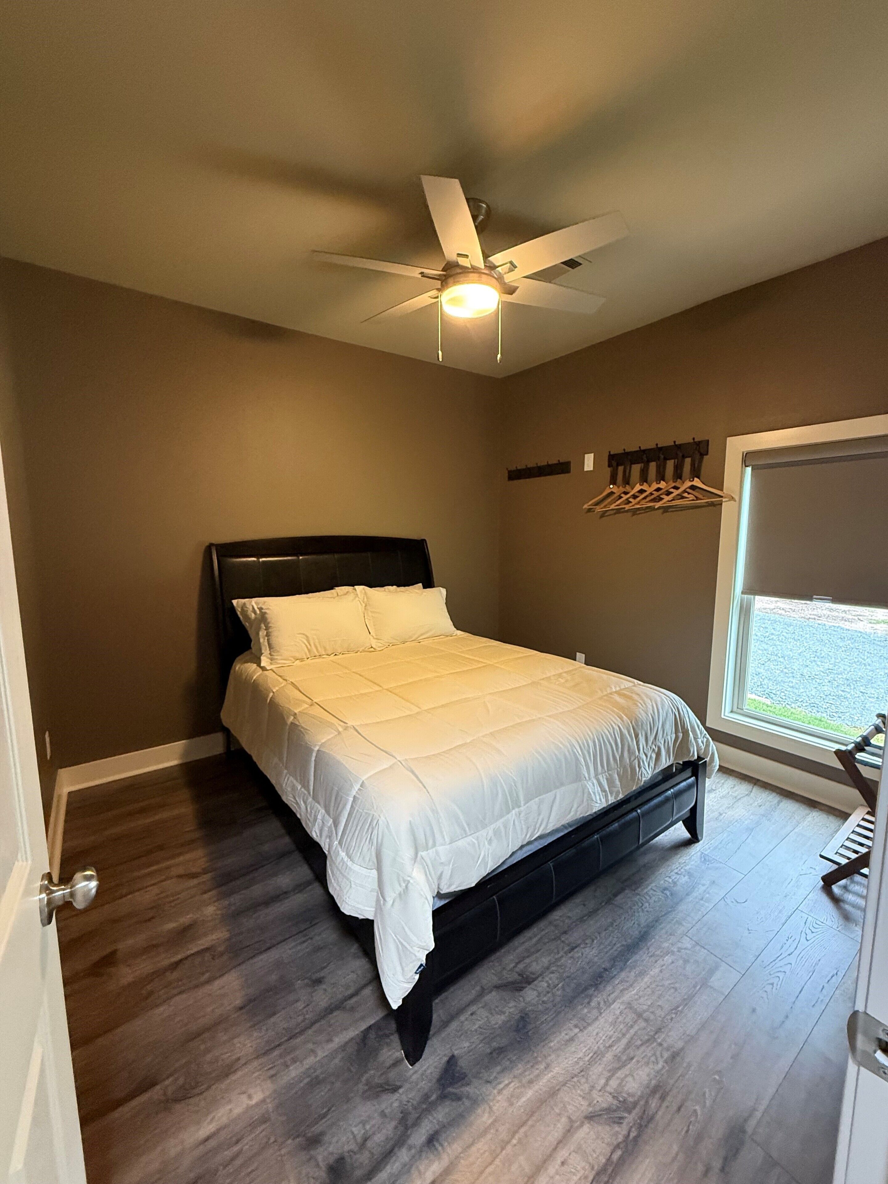 A bedroom with a bed, a ceiling fan, a window, and a door.