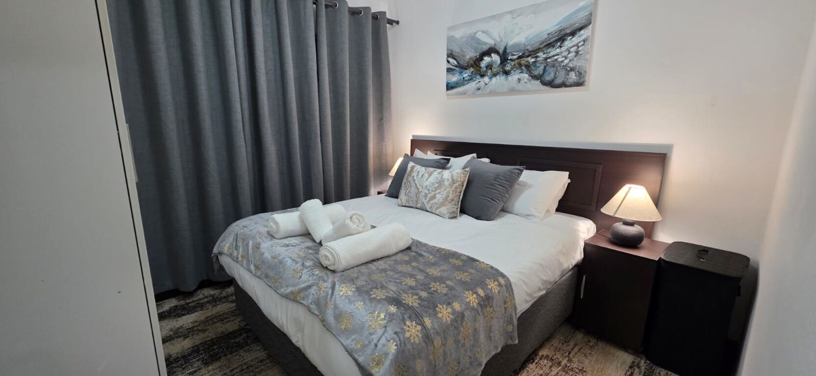 A hotel room with a bed, a nightstand, a lamp, and a painting on the wall.