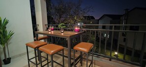 Ein Balkon im Freien mit Tisch und vier Stühlen, umgeben von einem Metallgeländer.
