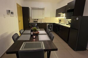 A modern kitchen with dark cabinetry, a dining table with chairs, a built-in oven, and a refrigerator. - Stylish 2BR Apartment, Pool & Balcony, Joburg (Midrand)