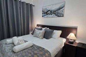 A hotel room with a bed, pillows, a lamp, and a painting on the wall. - Stylish 2BR Apartment, Pool & Balcony, Joburg (Midrand)
