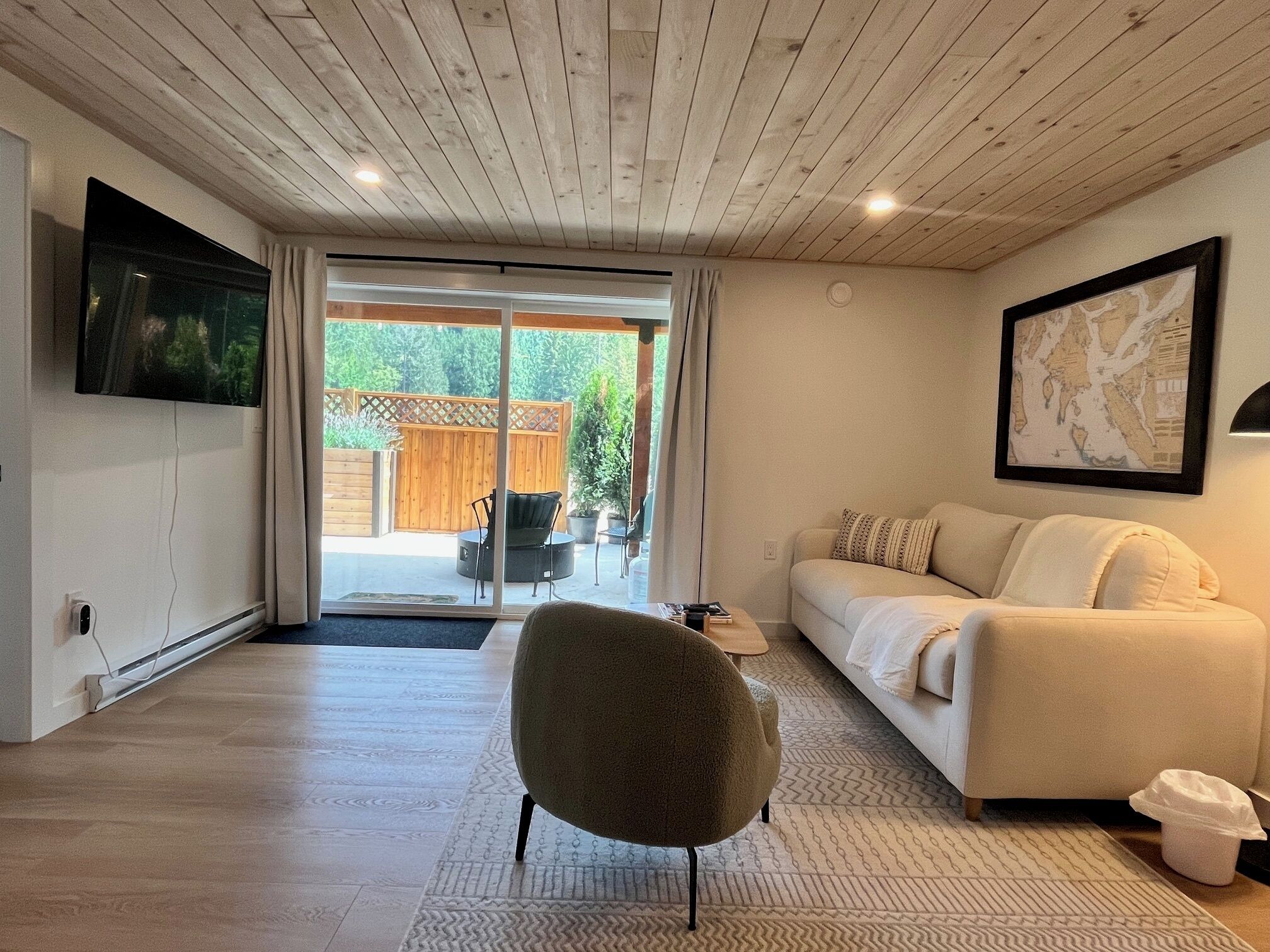 A modern living room with a sofa, a chair, a flat-screen TV, and a large window with a view of the outdoors.