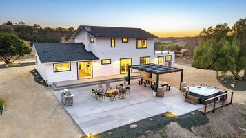 Una casa de dos pisos con un patio que cuenta con mobiliario exterior, un jacuzzi y una pérgola.