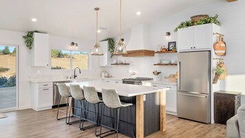 Una cocina moderna con una isla central, taburetes de bar, electrodomésticos de acero inoxidable y vistas al exterior.