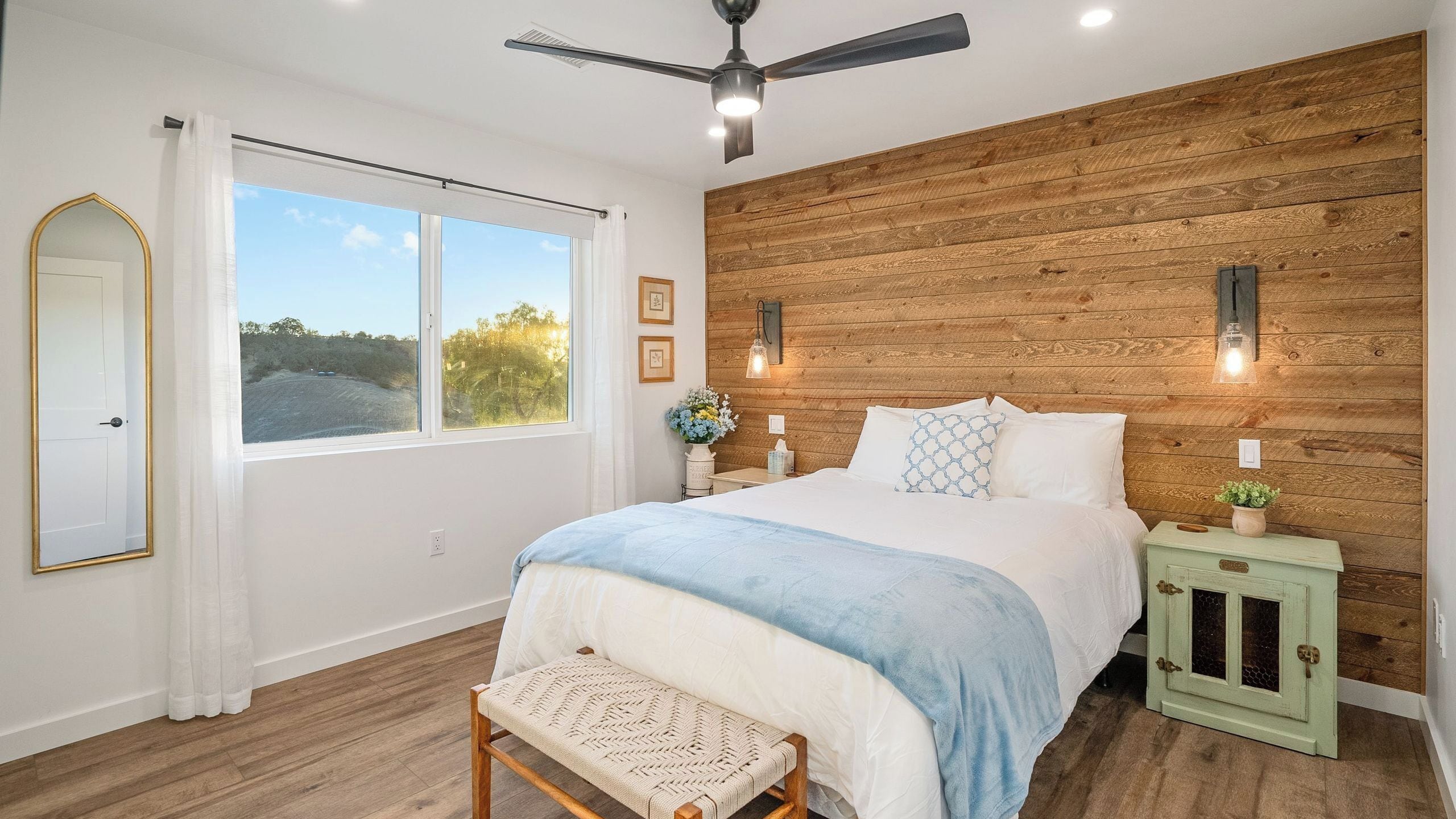A bedroom with a bed, a bench, a nightstand, a mirror, and a wooden wall.