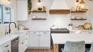 A modern kitchen with white cabinetry, a central island, and a stove. - The Shire at Baggins Hill by Avantstay Hot Tub + Playhouse + Cornhole 10 Private Acres (Templeton)