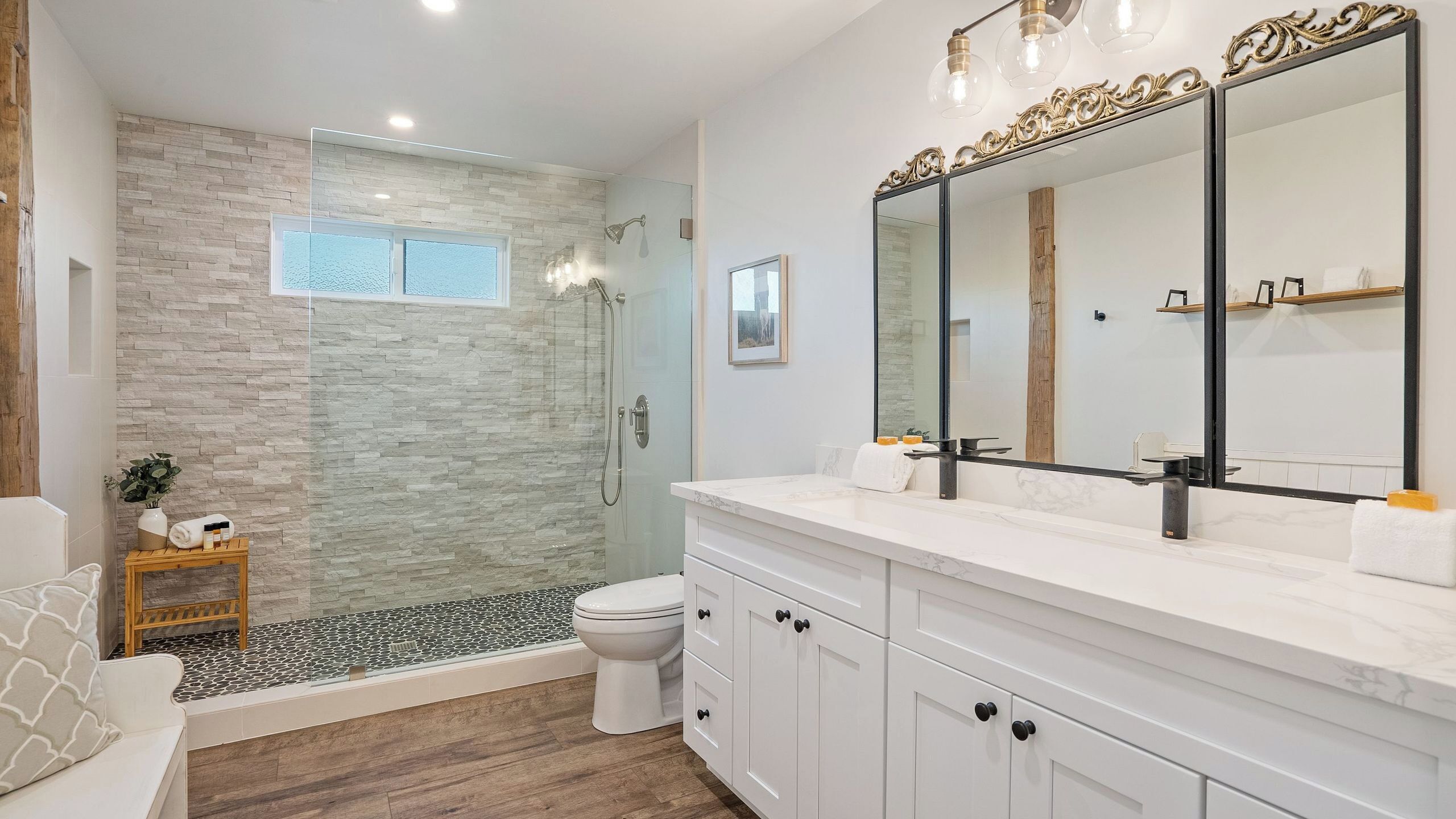 A modern bathroom with a glass shower enclosure, a toilet, a vanity with a large mirror, and a wooden floor.