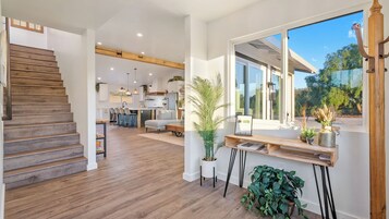 Amplia sala de estar con escalera de madera, cocina y un ventanal con vistas a la vegetación.